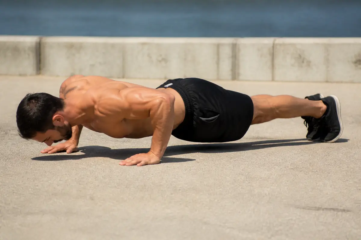 Homme faisant des pompes pour le dos sur sol extérieur avec détermination musculaire visible